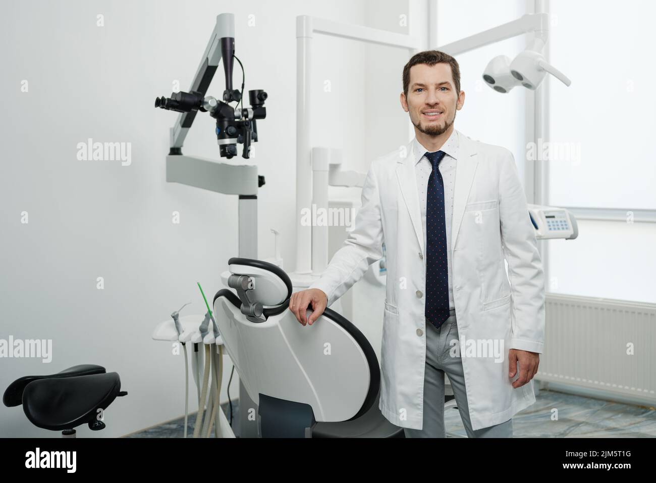 Portrait of happy male dentist wearing lab coat in white dental clinic