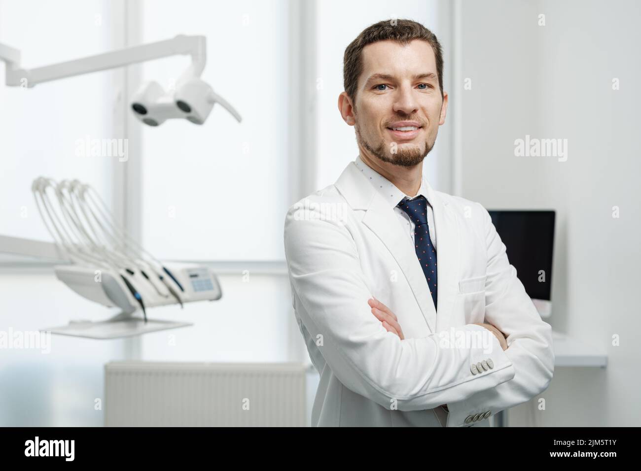 Happy male dentist in white lab coat posing with hands crossed and ...