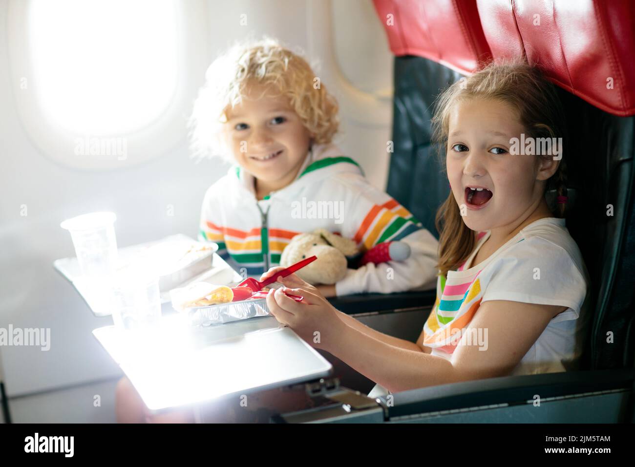 Child in airplane window seat. Kids flight meal. Children fly. Special inflight menu, food and drink for baby and kid. Stock Photo