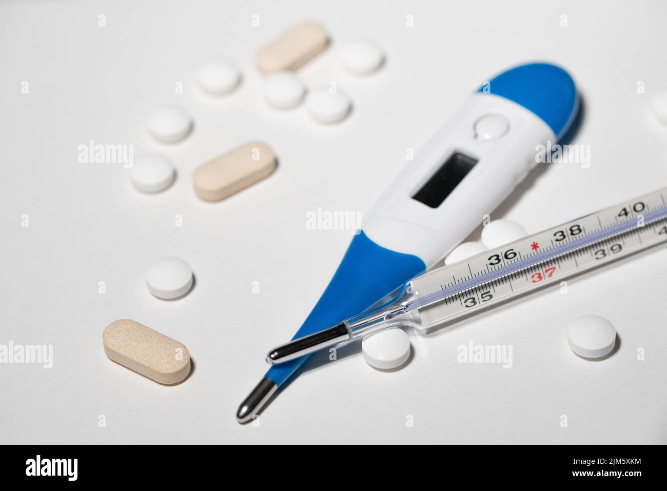 Analog and Digital thermometer on white surface with medicine and pills. Stock Photo