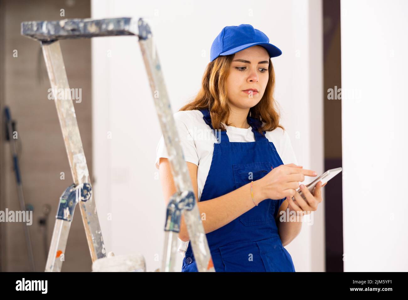 Female construction worker using smartphone in apartment Stock Photo