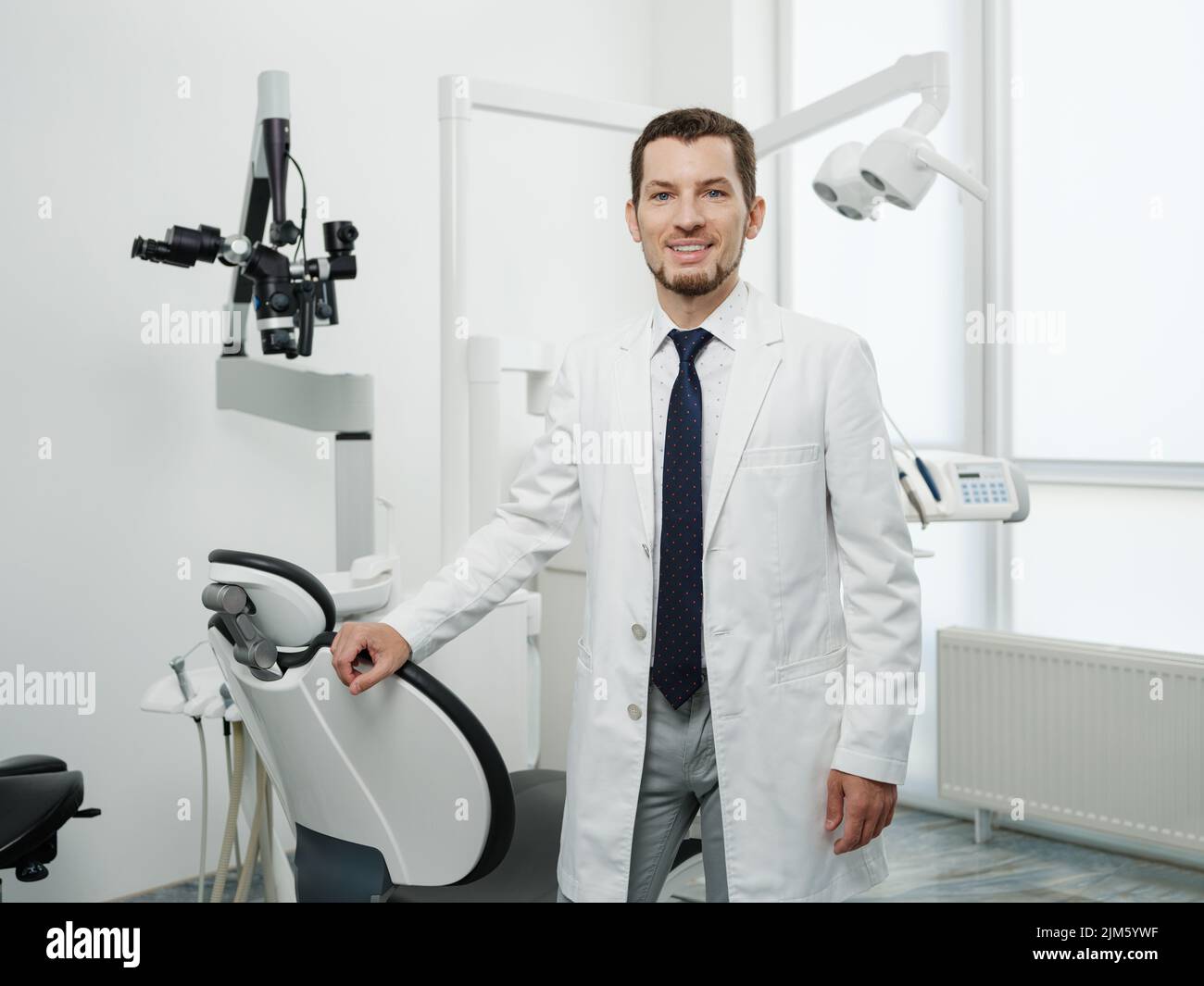 Portrait of happy male dentist wearing lab coat in white dental clinic