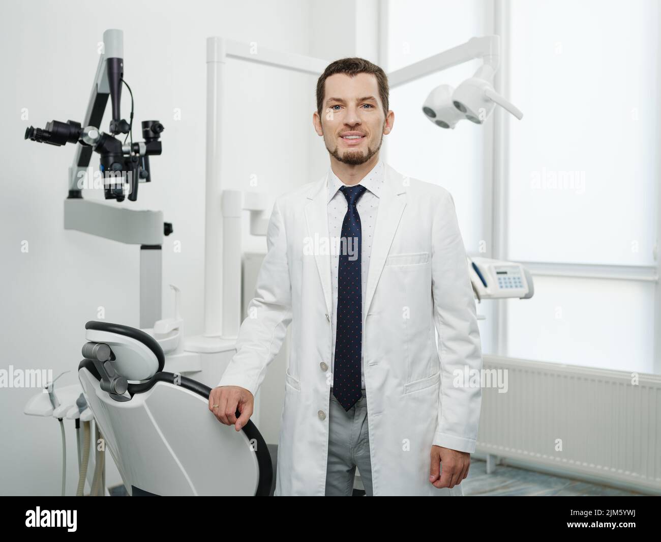 Portrait of happy male dentist wearing lab coat in white dental clinic