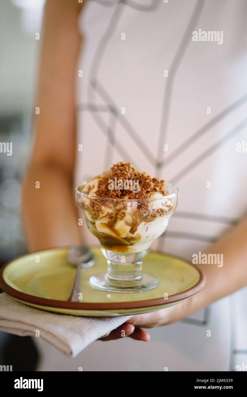 A closeup shot of a woman holding plate has glass cup of ice cream with nuts and spoon Stock Photo