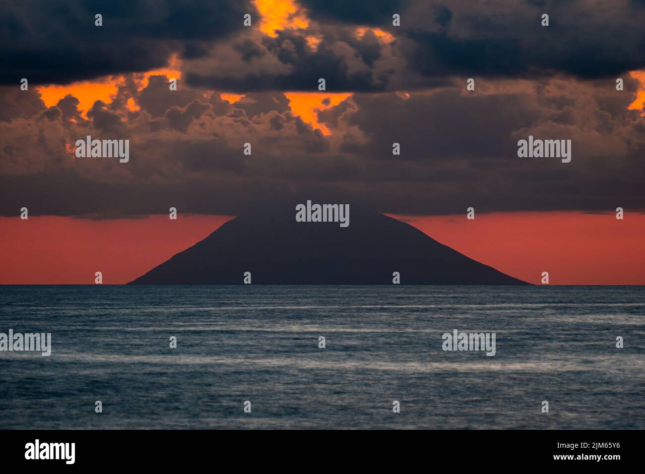 A beautiful view of the sea under the cloudy sunset sky with a hill in ...