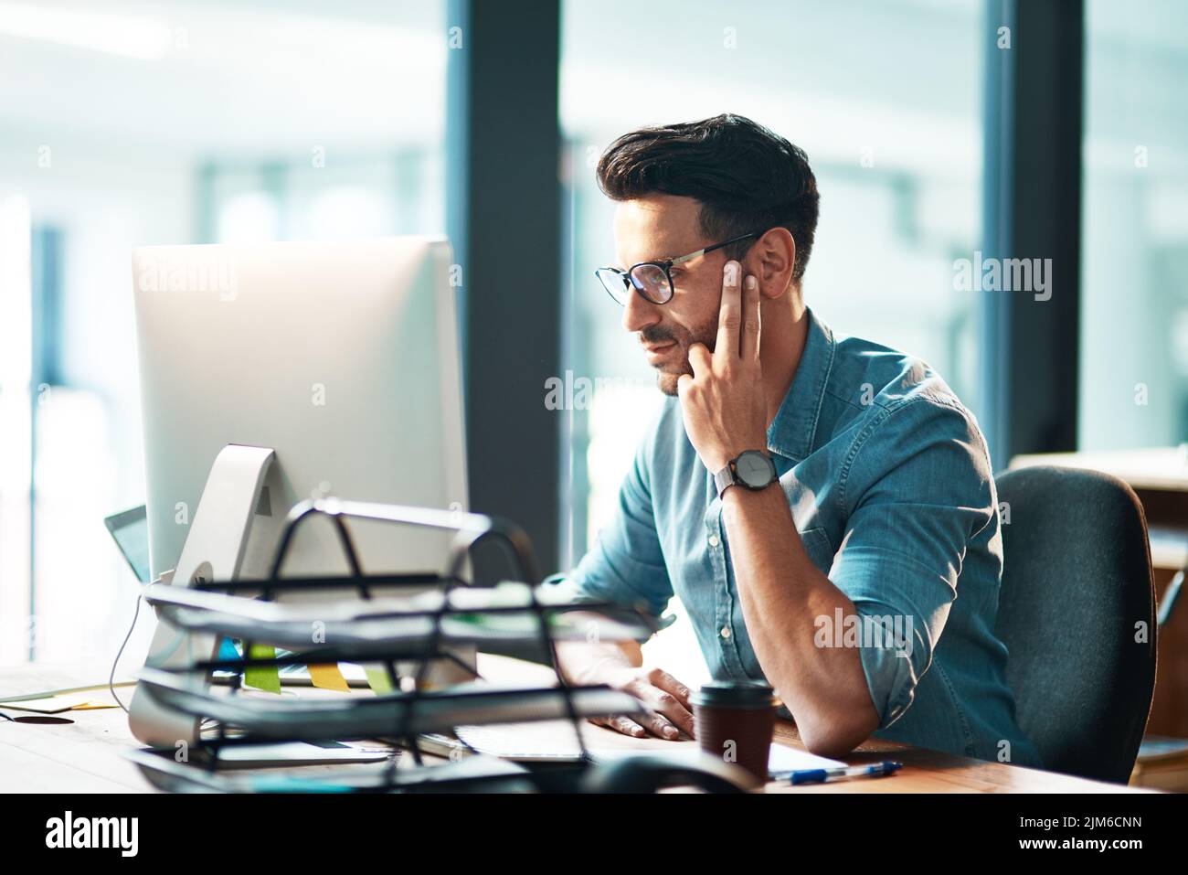 Professional corporate business man working on computer, browsing the internet and completing a project while sitting at a desk alone at work. One Stock Photo