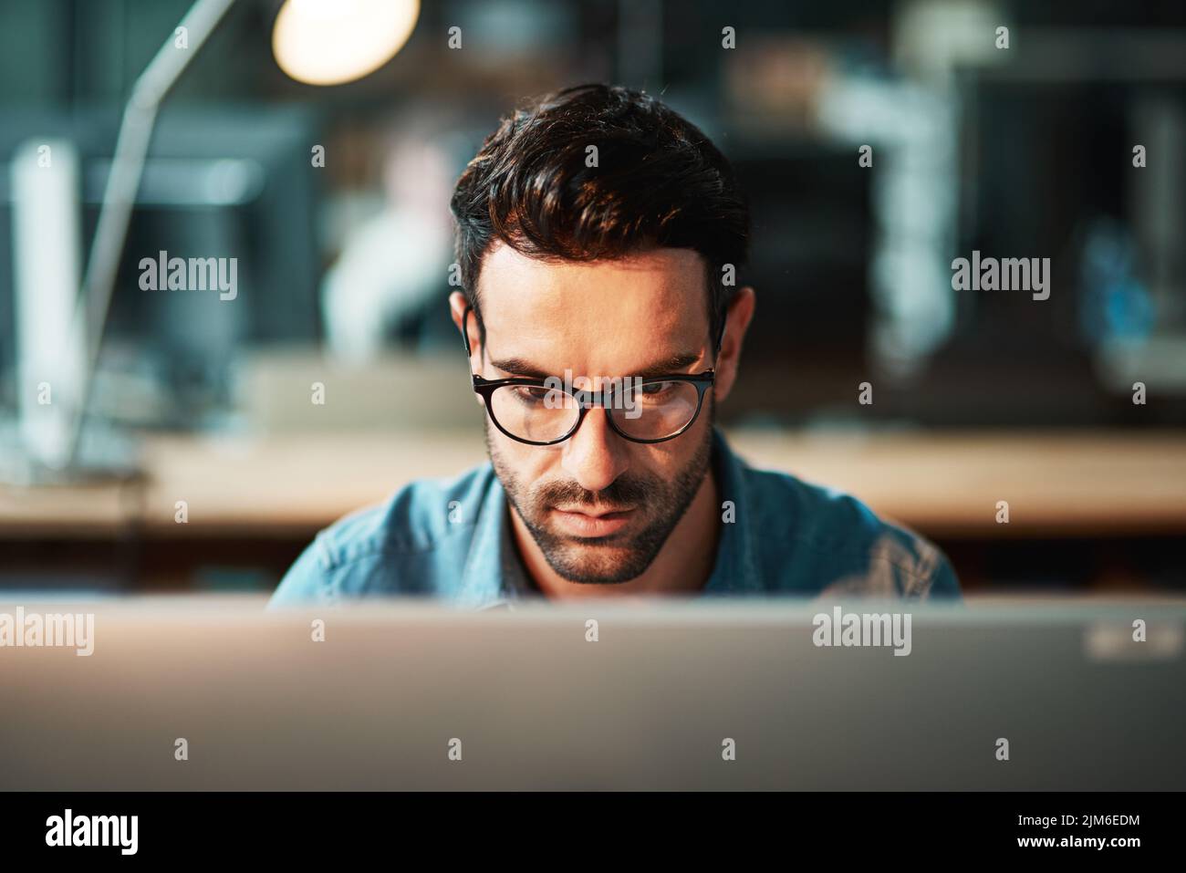 Serious business man working at computer late in the office at night to finish reports, articles or code. Focused and young male IT worker wearing Stock Photo