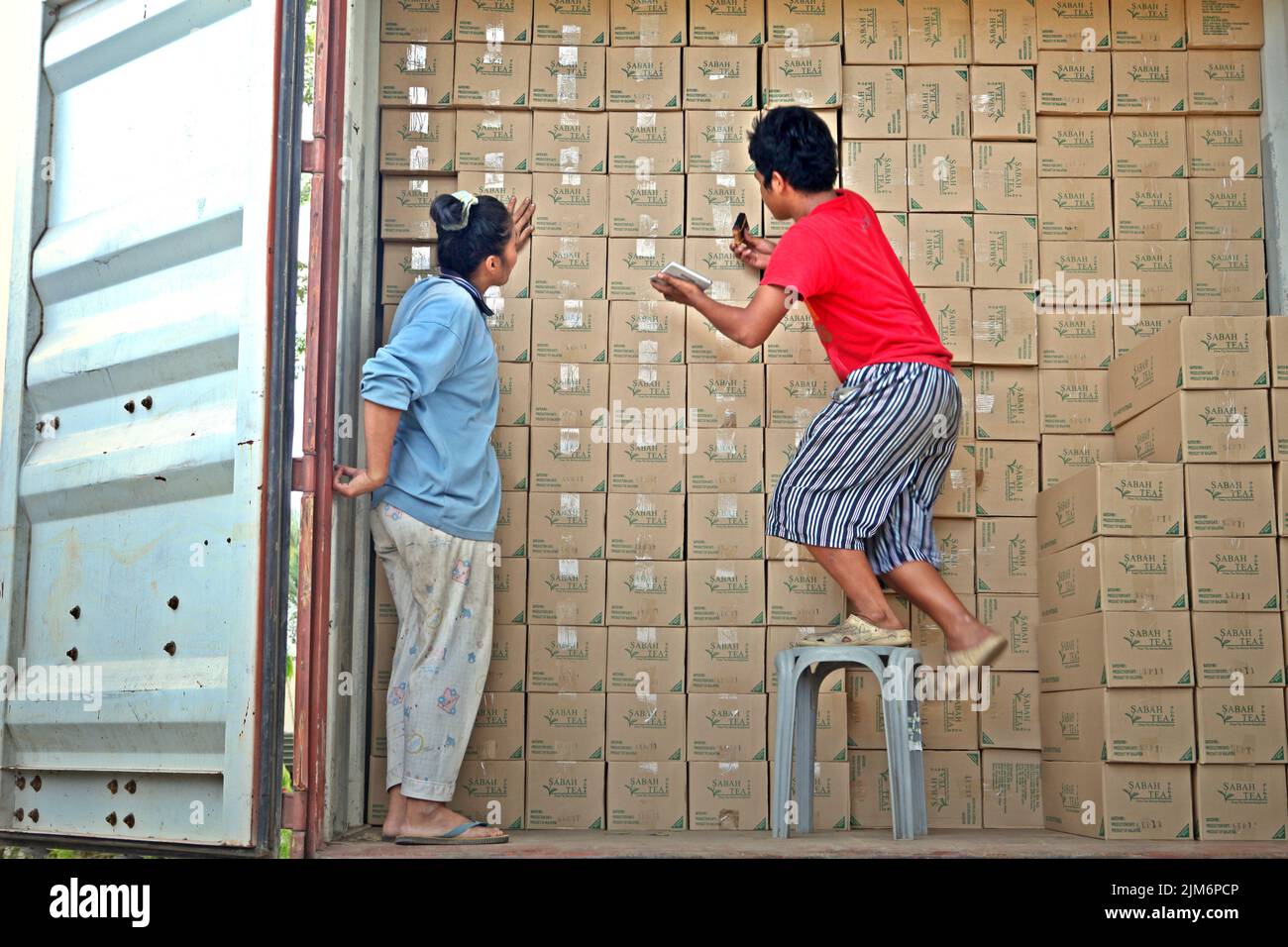Workers organizing paper boxes containing Sabah Tea for shipment, as they are standing inside a container truck at Sabah tea factory, the processing plant for materials harvested from organic tea farm, a part of Sabah tea garden in Sabah, Malaysia. Stock Photo