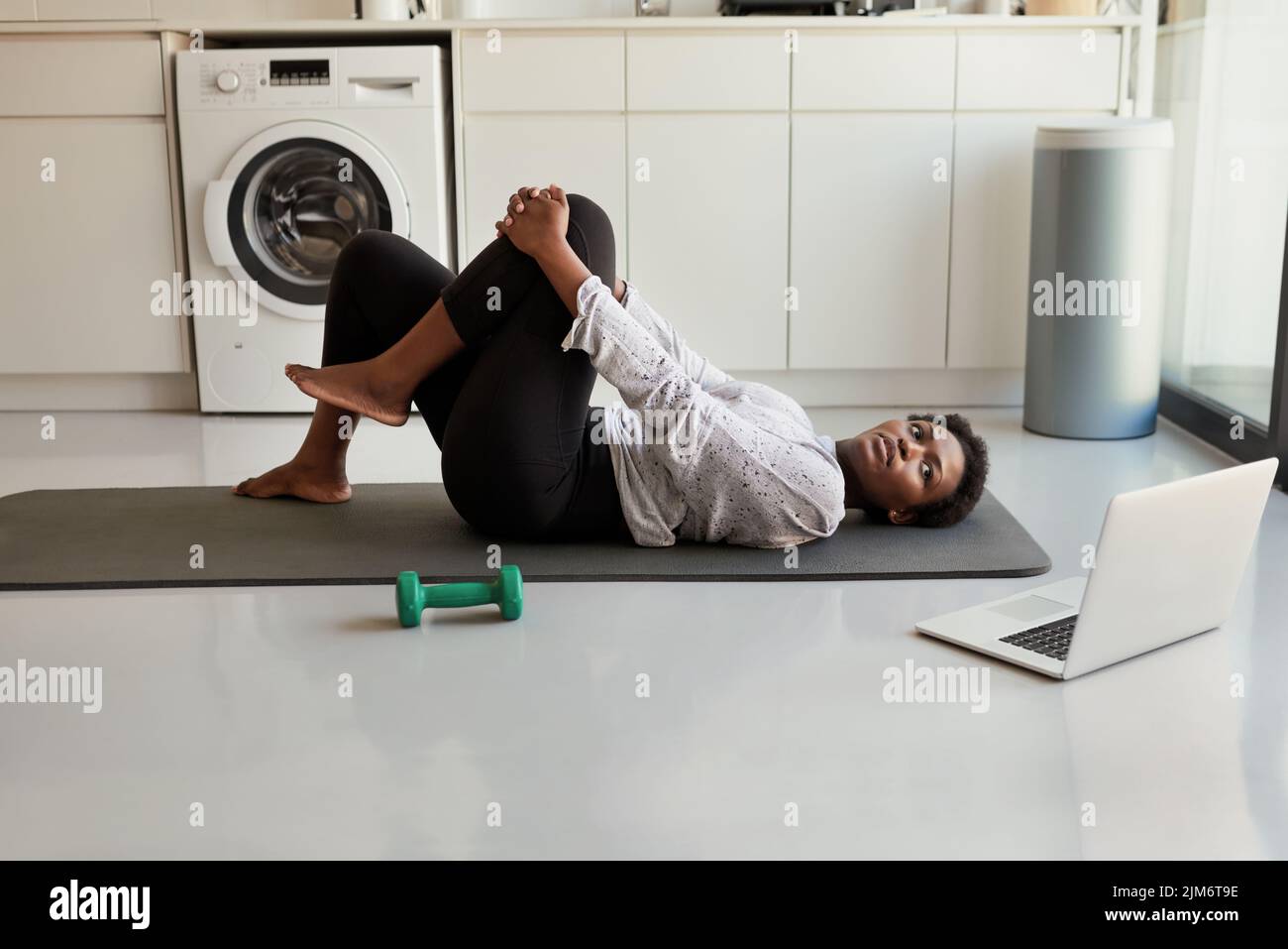 Am I doing this right. a young woman using a laptop while exercising at home. Stock Photo