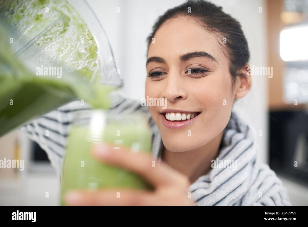 This will make me feel energised and ready for the day. a woman drinking a smoothie at home. Stock Photo