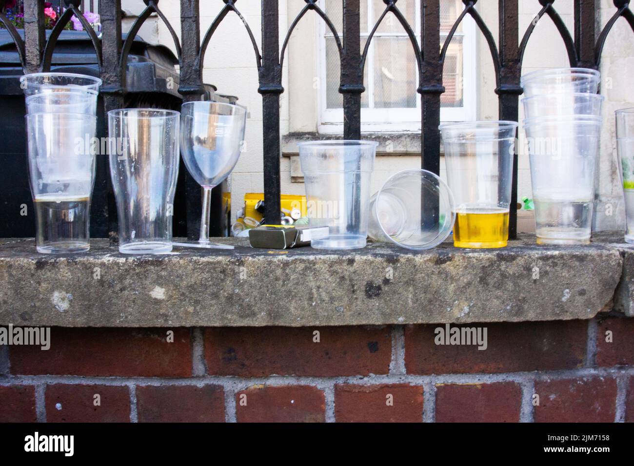 A closeup of plastic and glass cups on the brick wall surface against the metal railings. Stock Photo