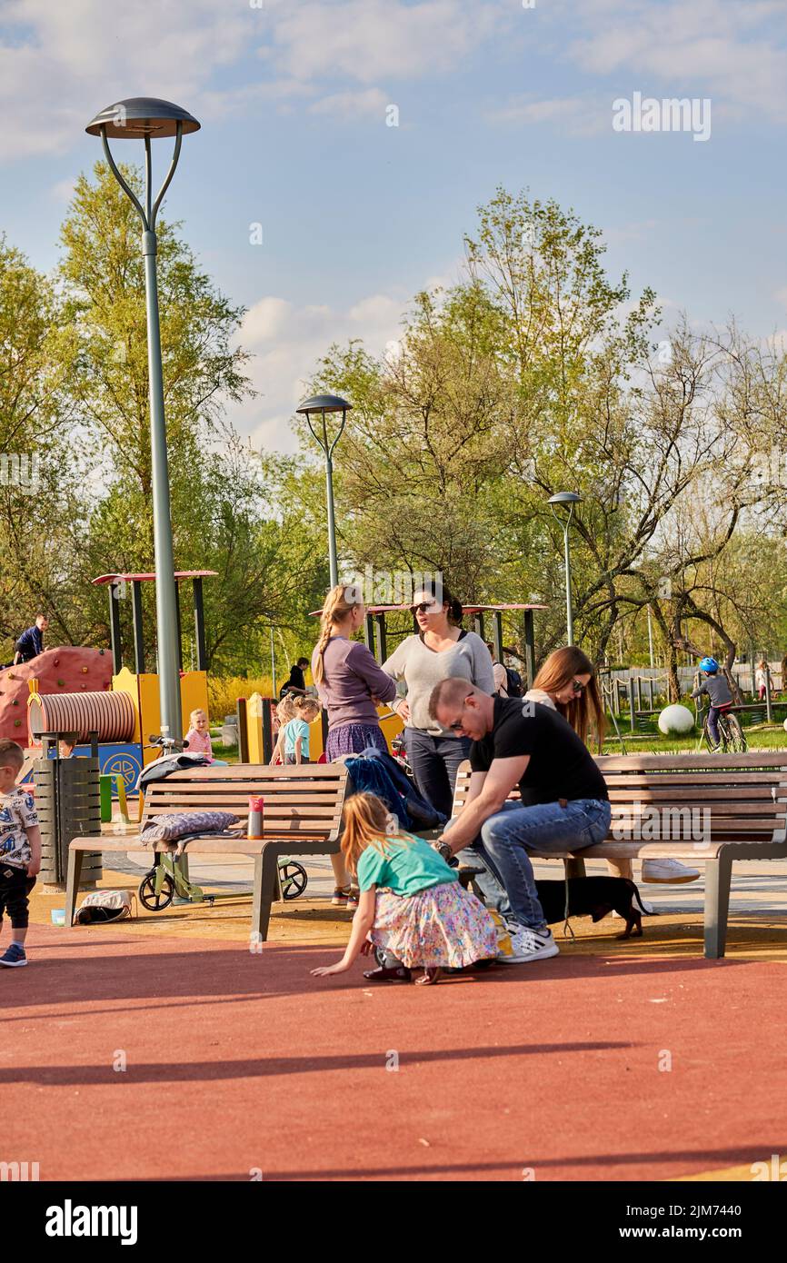 A group of adults and children around a wooden bench in the Rataje park on a warm spring day Stock Photo