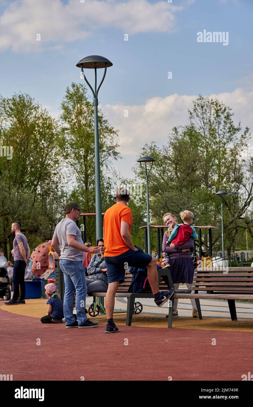 A group of adults and children around a wooden bench in the Rataje park on a warm spring day Stock Photo