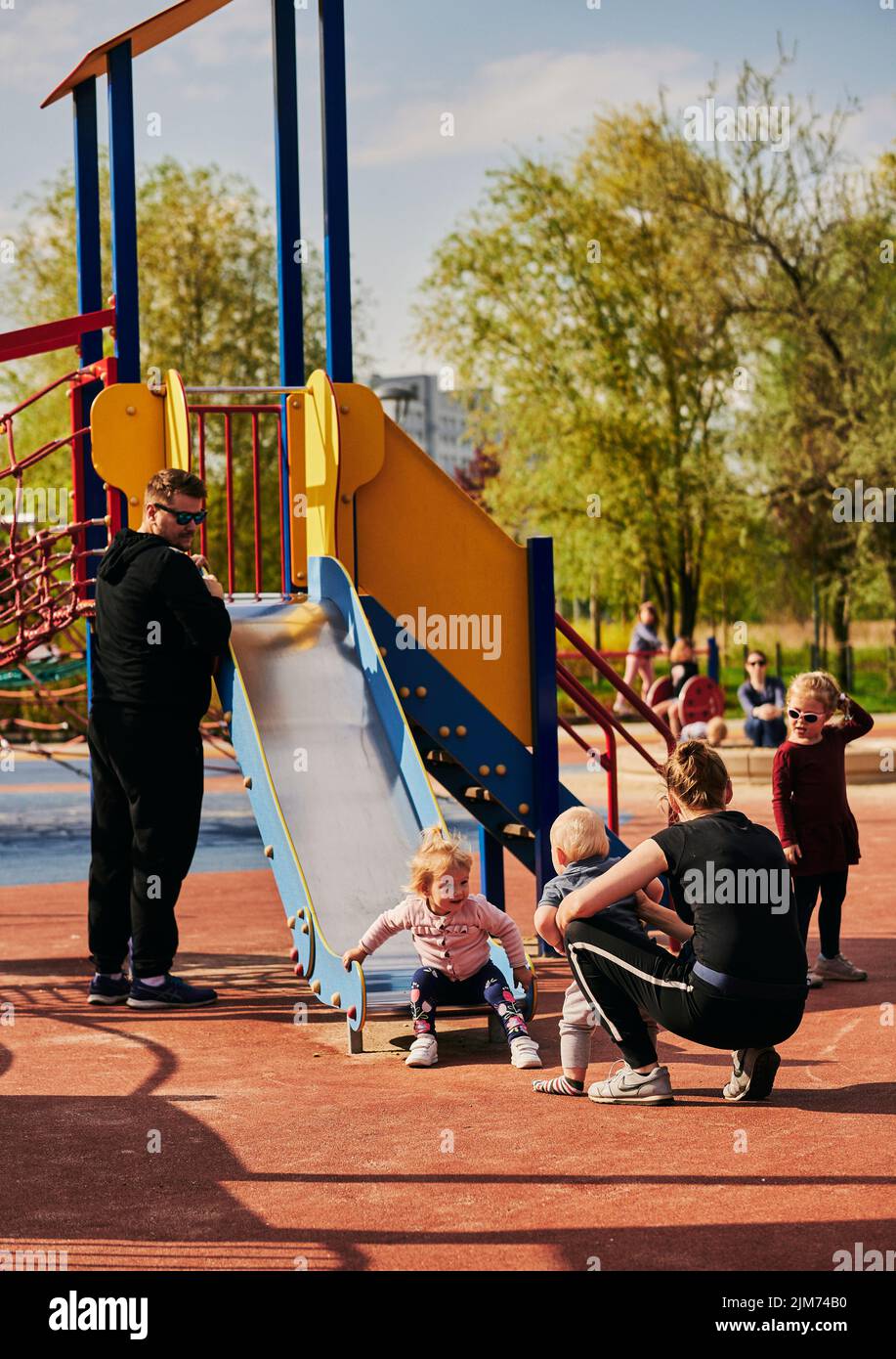 The parents standing by their children playing on the slide in the playground in Rataje park Stock Photo