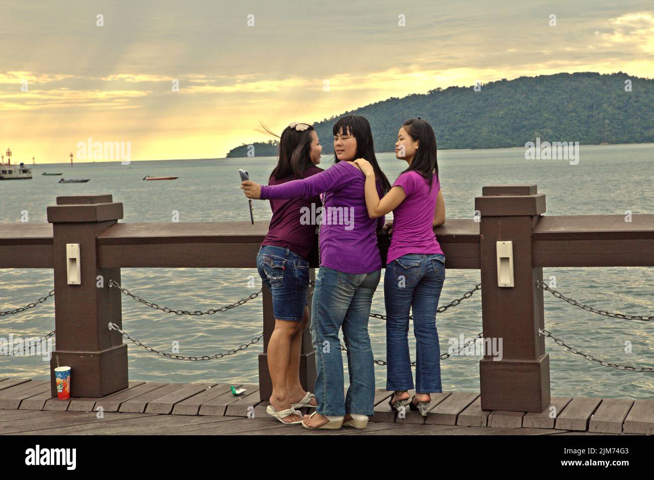 Young women taking selfie photo in a background of seascape view as they are having a leisure time on a seaside viewing platform in Kota Kinabalu, Sabah, Malaysia. Stock Photo