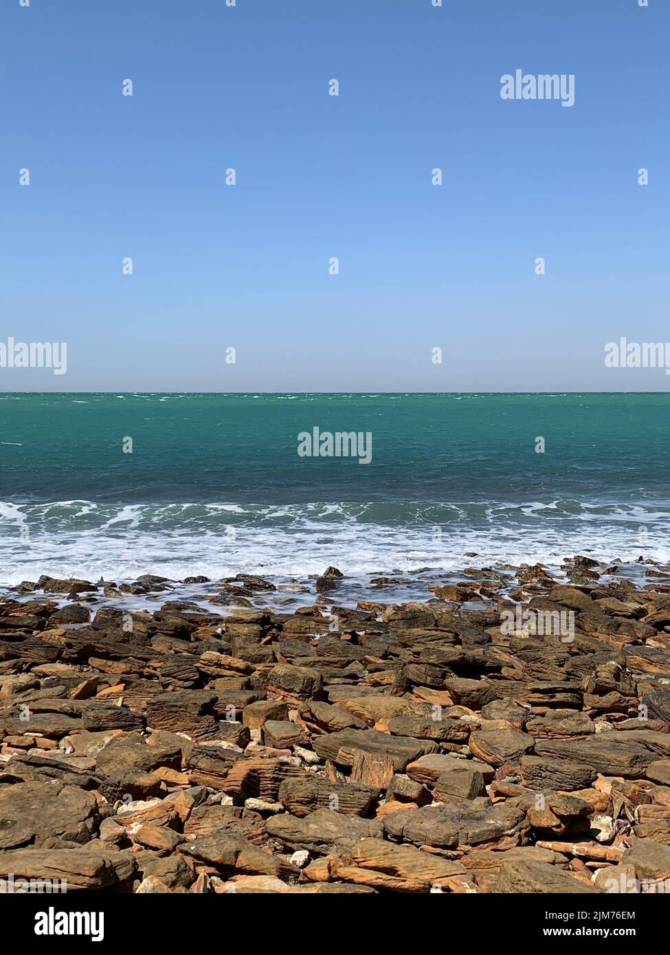 A vertical shot of a rocky beach with sea under clear sky Stock Photo ...