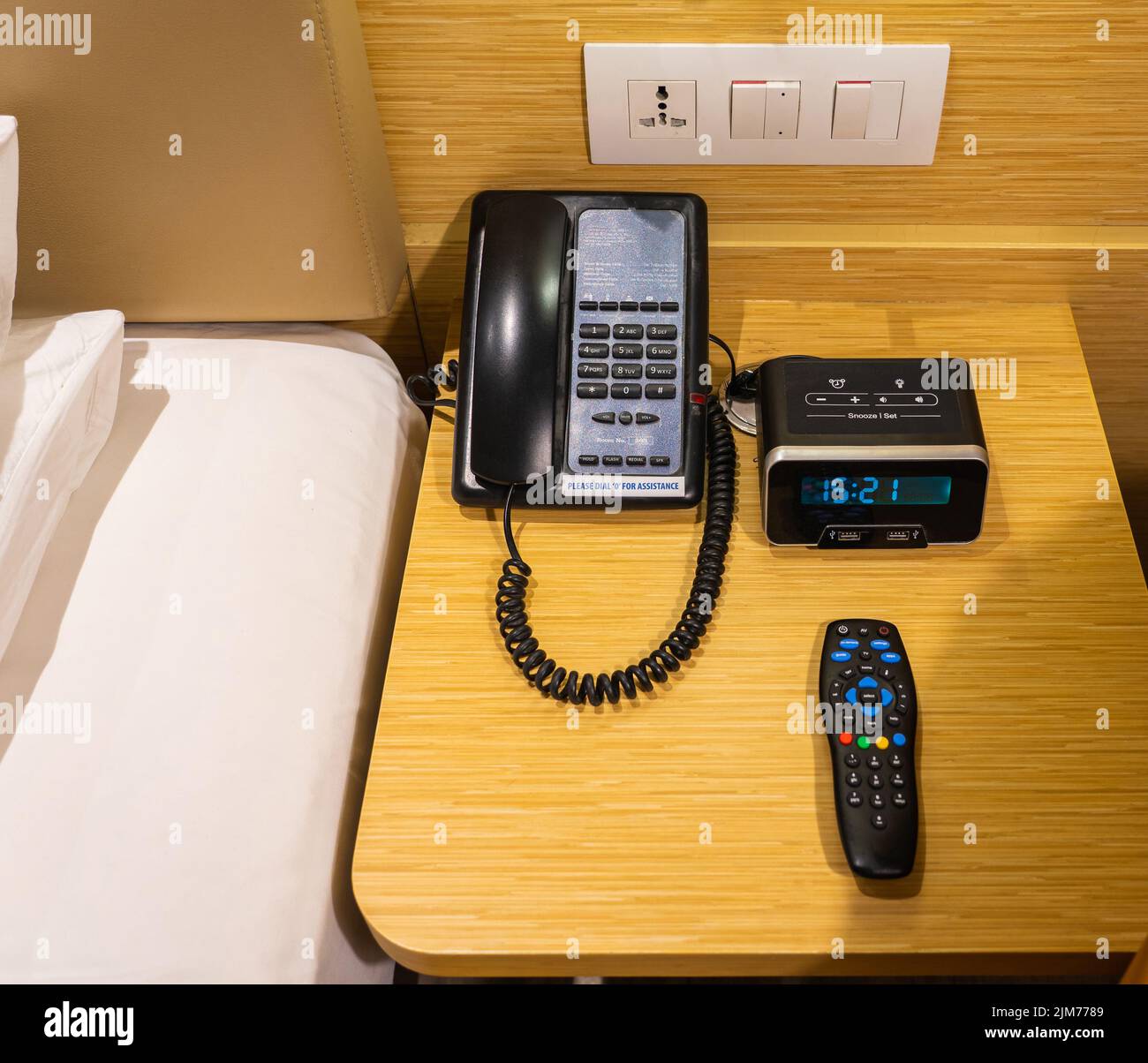 A telephone, digital clock, and a television remote control by the bedside Stock Photo