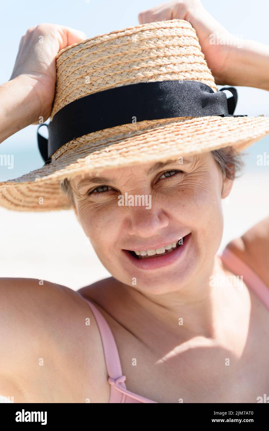 Woman lightheartedly laughing at the camera while holding a straw hat