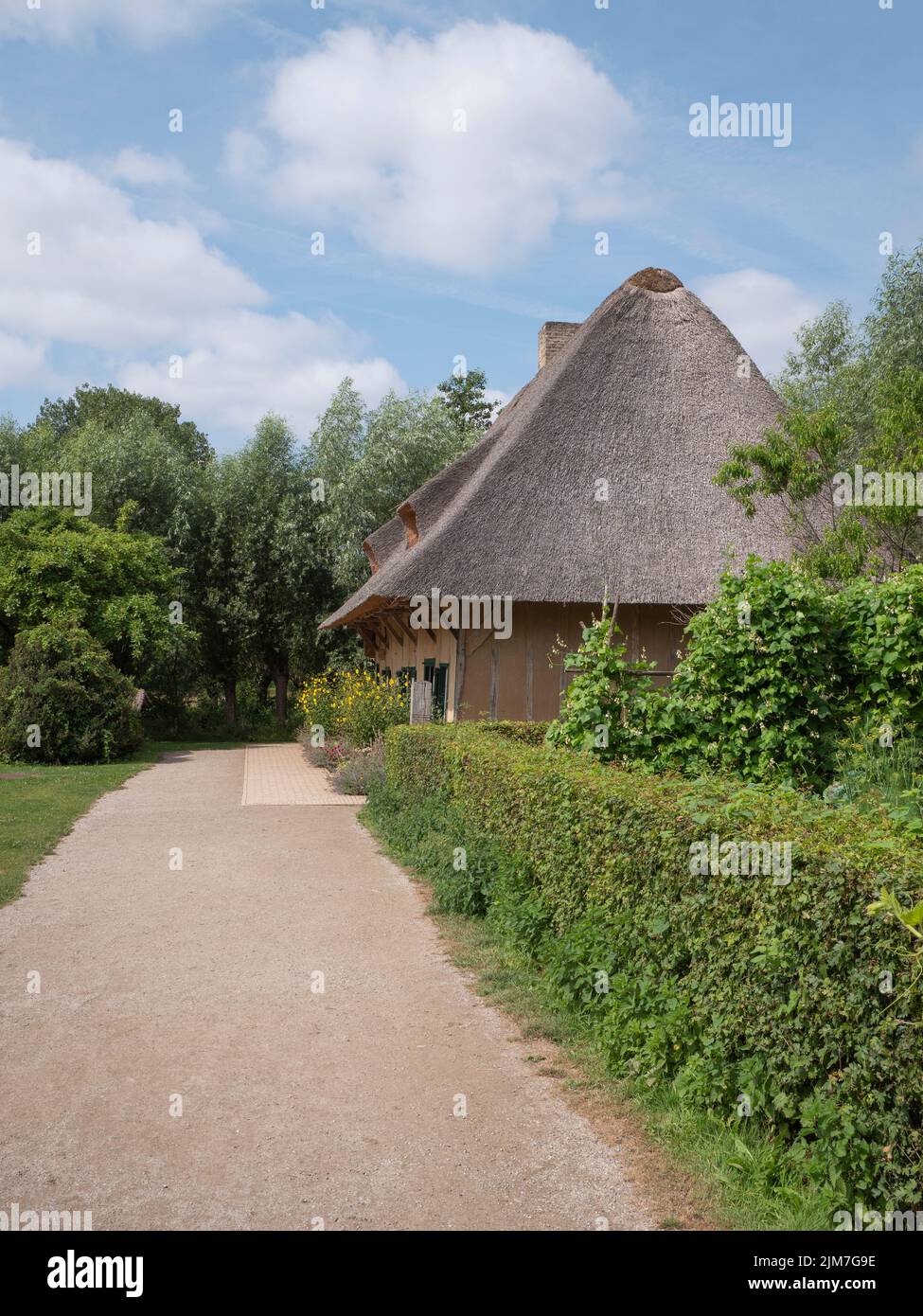 Dusty road to an old house with a large thatched roof from the province of West Flanders in Belgium located in Bokrijk Stock Photo