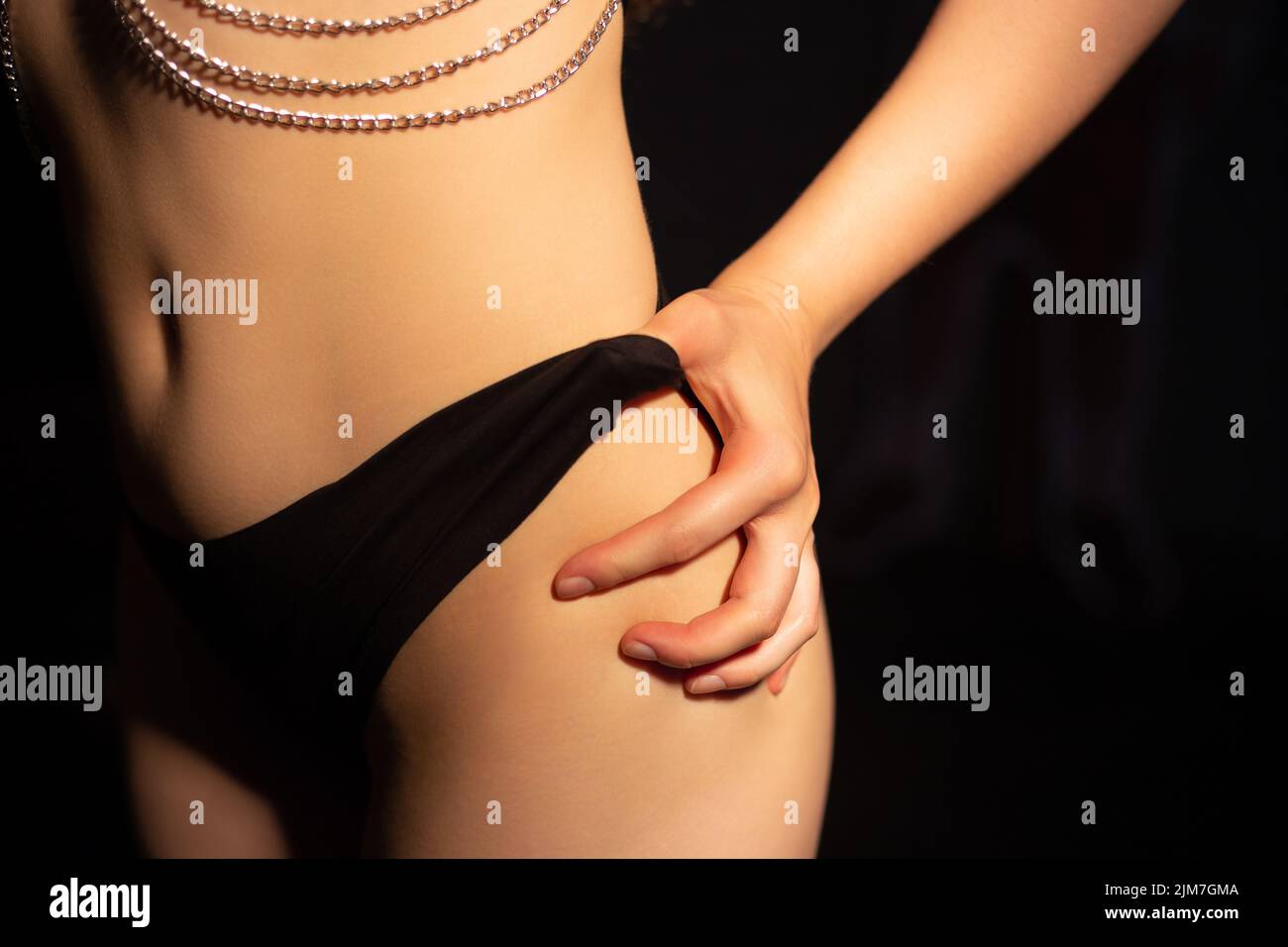 Photo of woman with chains in black lingerie in shadowon black background Stock Photo