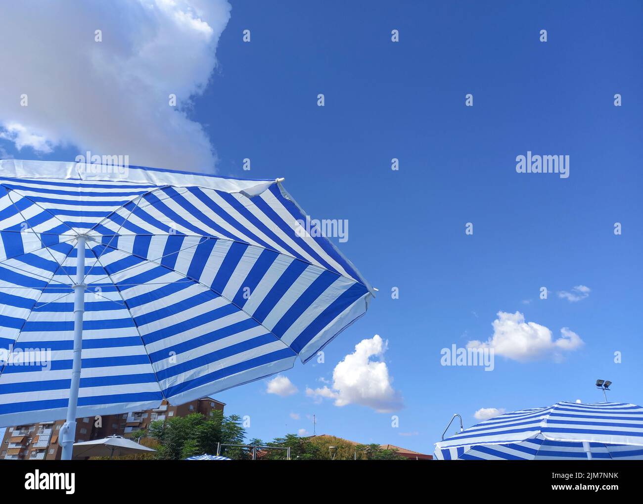 Blue striped umbrellas over blue sky with apartment building. Urban swimning pool background Stock Photo