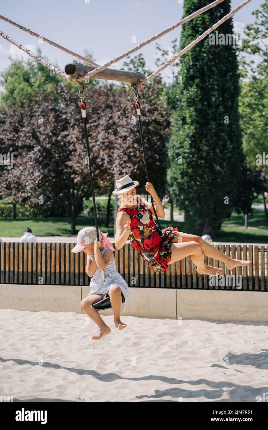 Mother and daughter in a swing having fun at the park playground. Mom