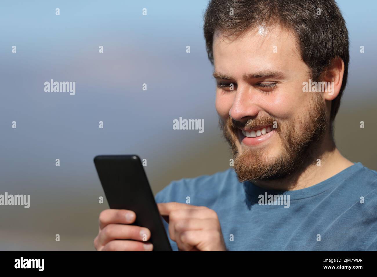 Close up of a happy man using mobile phone a sunny day Stock Photo
