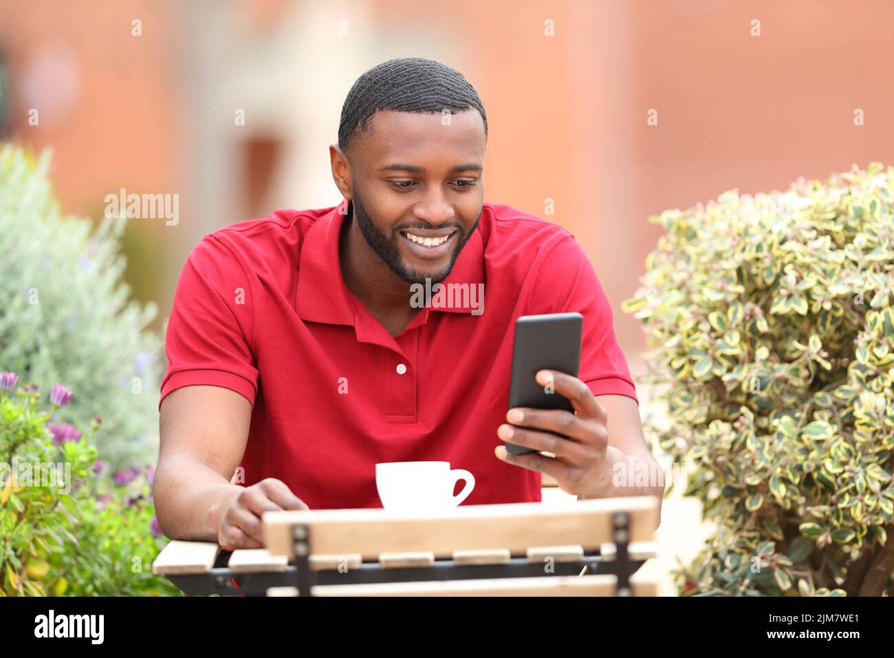 Happy man in red using smart phone sitting in a coffee shop terrace Stock Photo