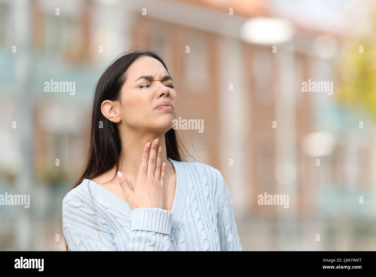 Stressed woman suffering sore throat standing in the street Stock Photo