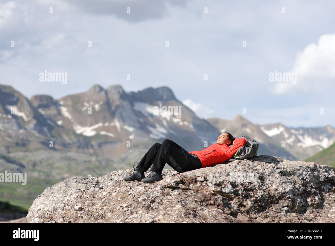 Tired hiker in red resting lying and relaxing on the top of a high mountain Stock Photo