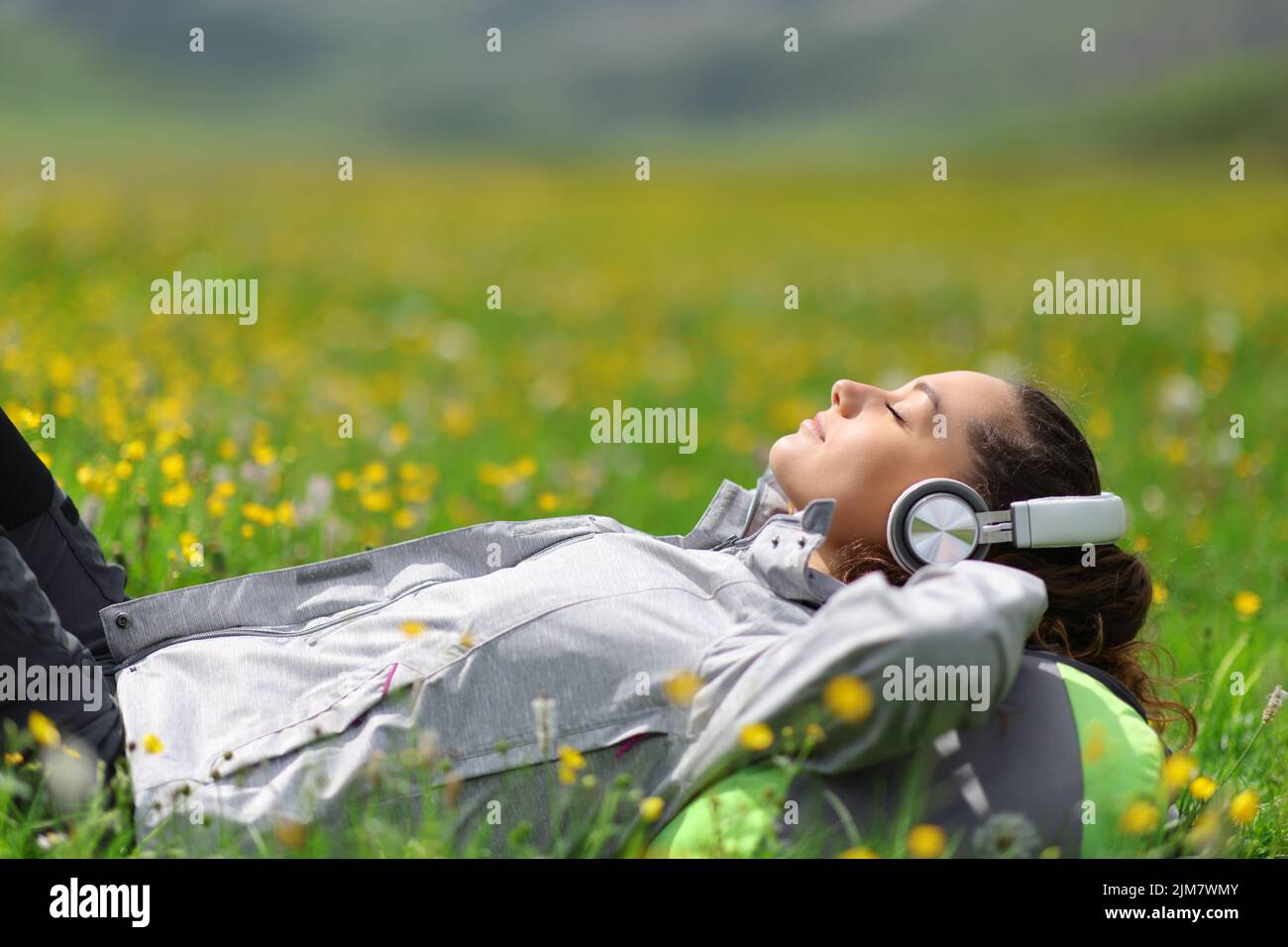 Hiker wearing headphones listening to music relaxing lying on the grass in a field in the mountain Stock Photo