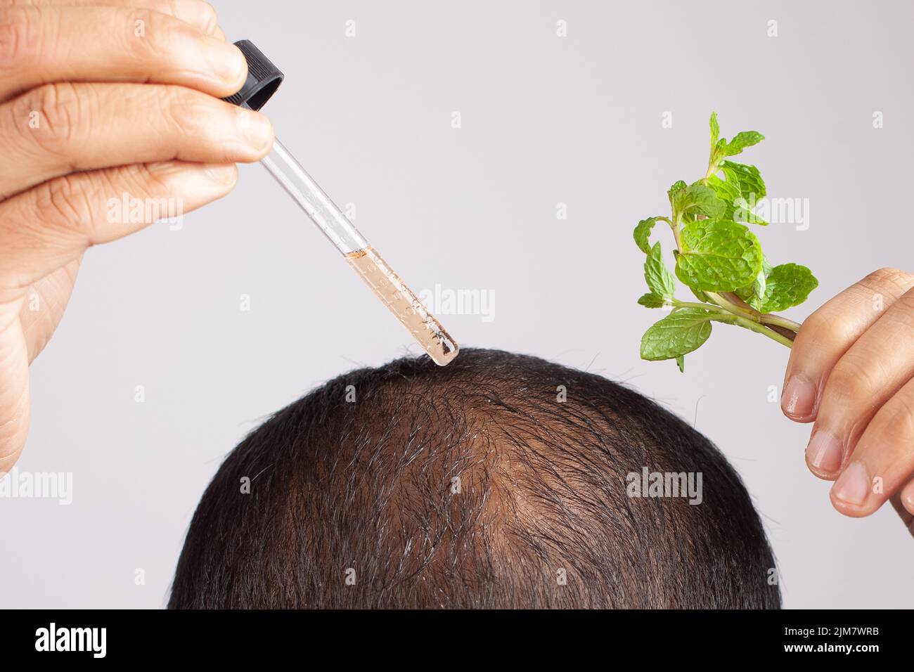 Man holding peppermint oil dropper applying on scalp to promote hair