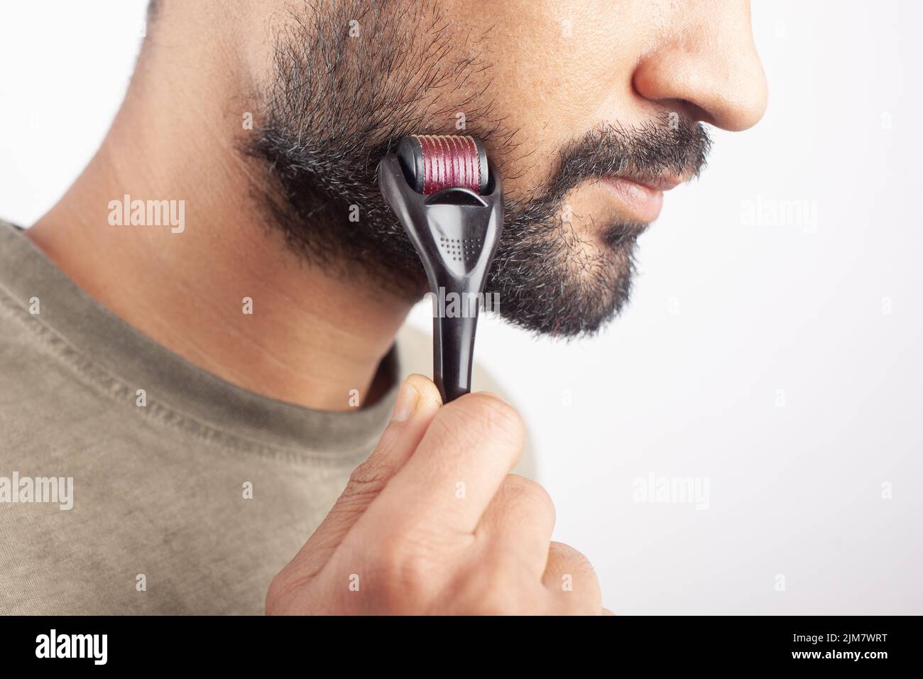 White background young Caucasian male using dermaroller on beard for beard  growth Stock Photo - Alamy