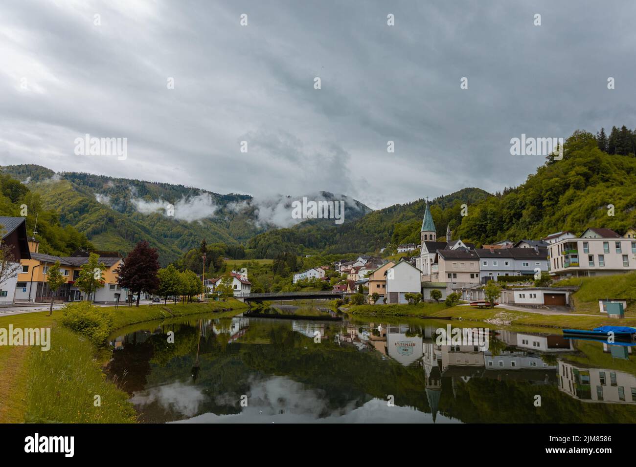 Panorama of the city of Reichraming a small town in central austria on a cloudy day. Visible reflection of the village over the river running through Stock Photo