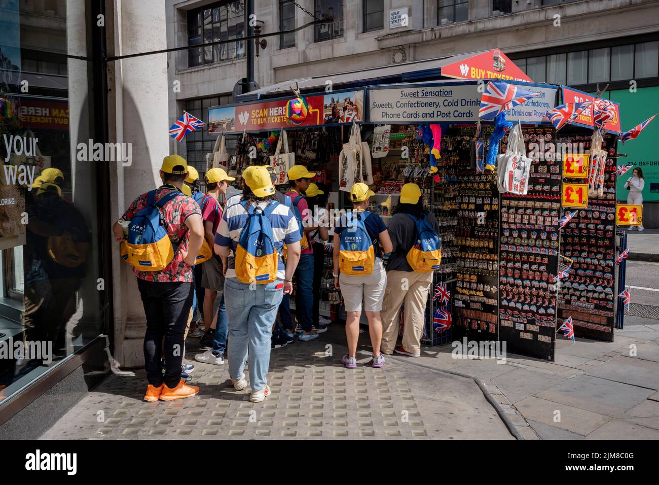 A tour group wearing identical yellow hats stand at a tourist souvenir kiosk in Regent Street in the West End, on 3rd August 2022, in London, England. Stock Photo