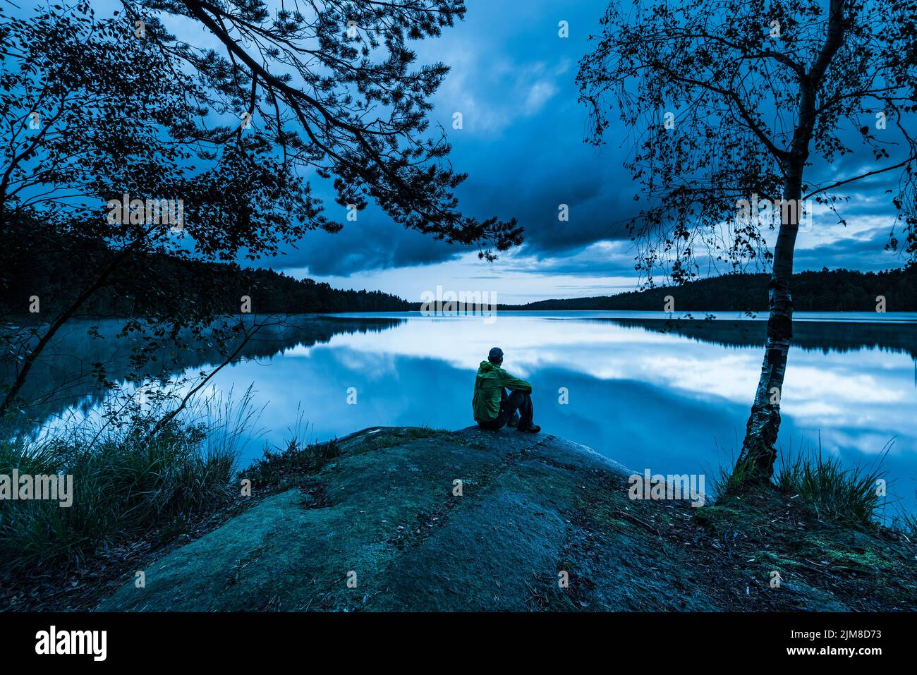 Lonely man sitting besides lake at blue hour Stock Photo