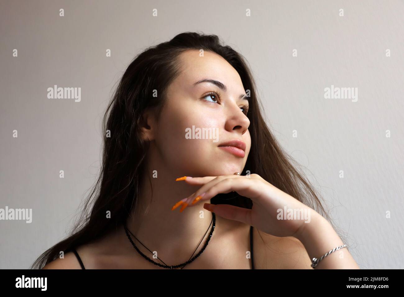 Portrait of attractive young girl with long hair touching her dreaming face with her hand with orange acrylic nails. Female beauty, skin care Stock Photo