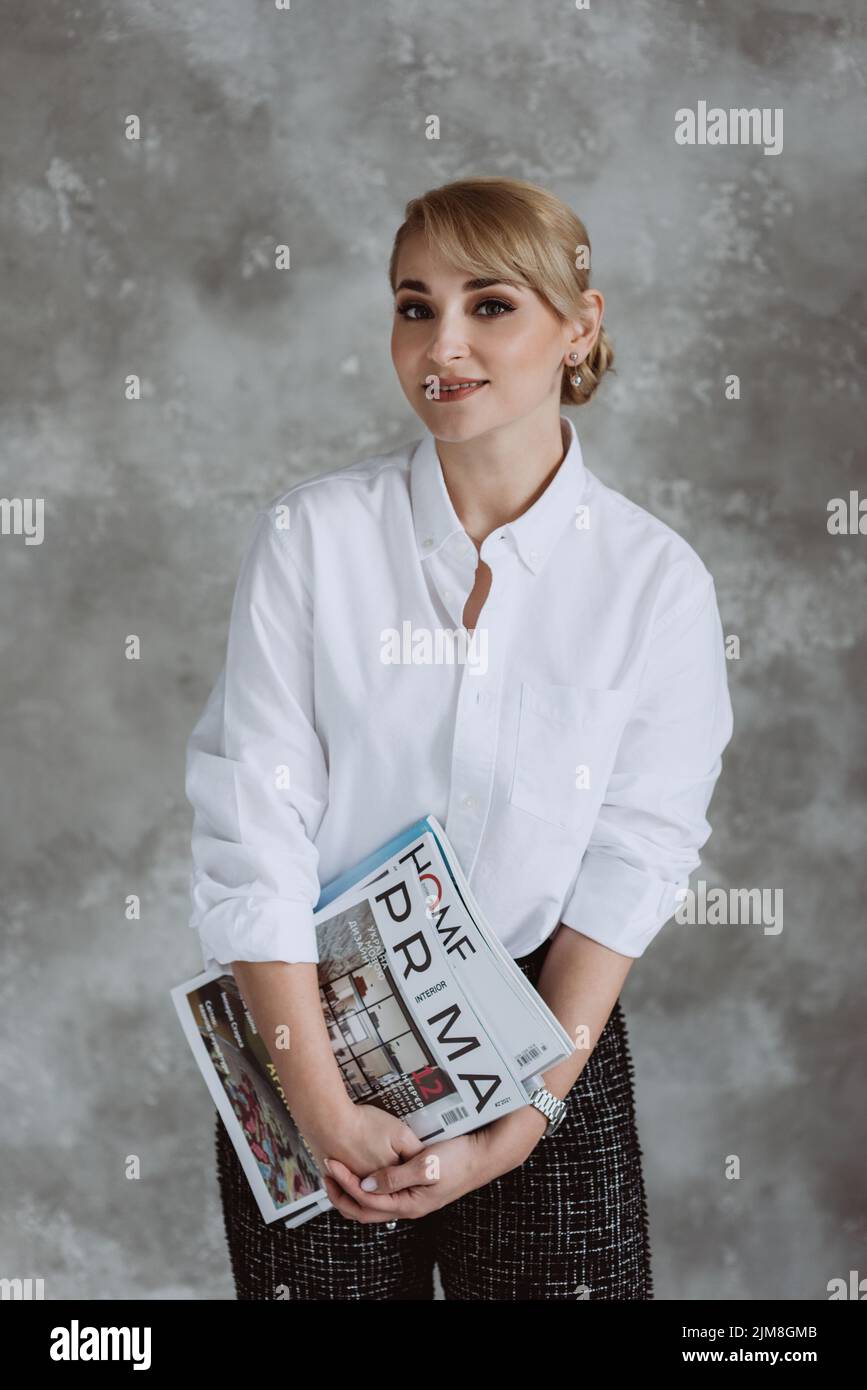 Kyiv, Ukraine, 18 february 2022. Beautiful female interior designer with professional magazines in her hands, stands on a gray background. Soft select Stock Photo