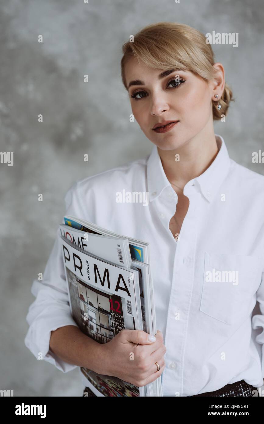 Kyiv, Ukraine, 18 february 2022. Beautiful female interior designer with professional magazines in her hands, stands on a gray background. Soft select Stock Photo