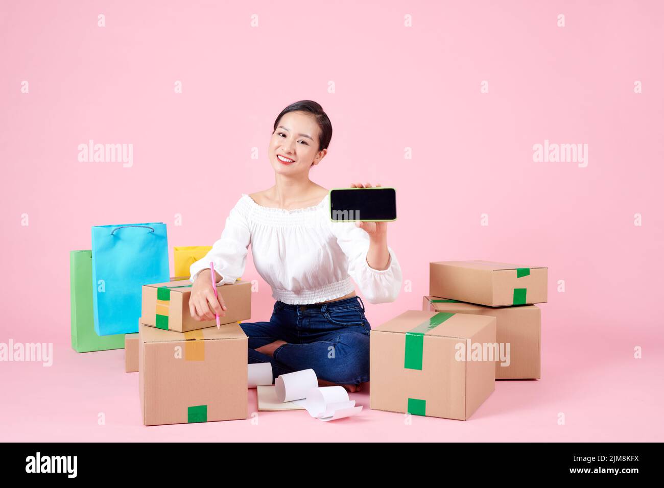 online shopping concept - Happy asian woman shows green screen smartphone with many parcels at home Stock Photo