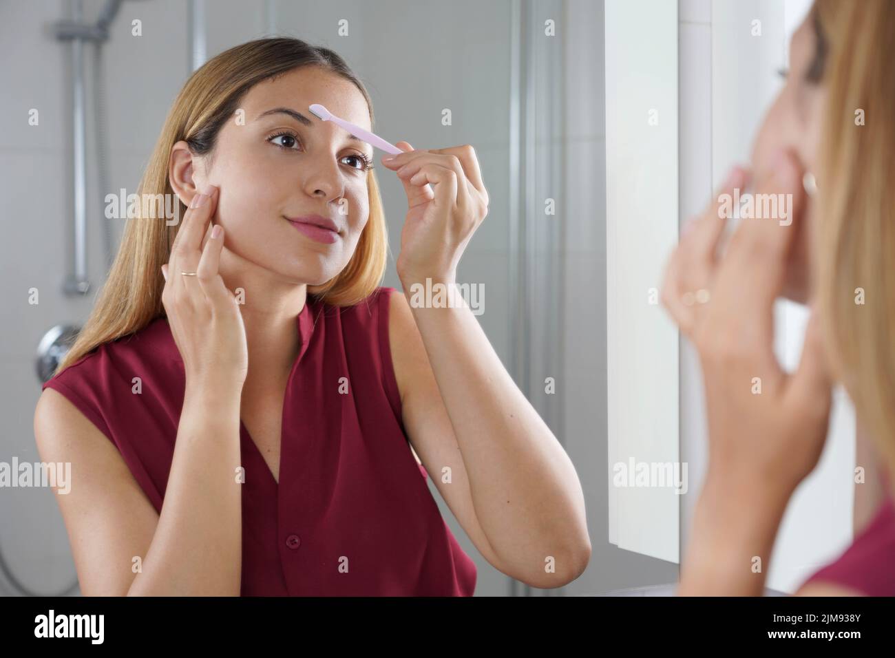 Facial hair removal. Beautiful young woman shaving her face by razor at
