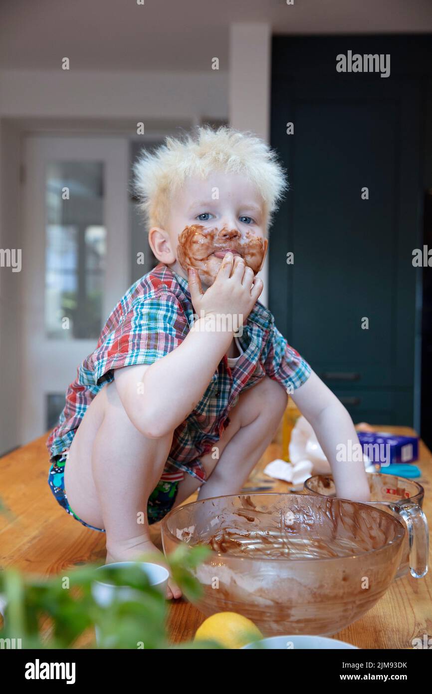 A young boy with hands and face covered in chocolate after helping in the kitchen to bake a cake Stock Photo