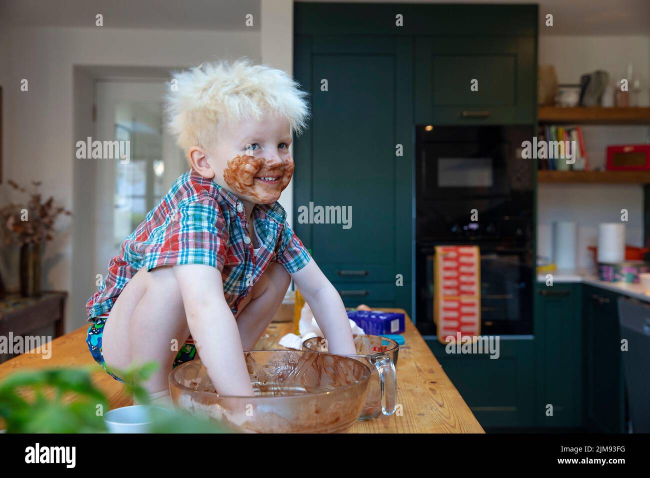 A young boy with hands and face covered in chocolate after helping in the kitchen to bake a cake Stock Photo