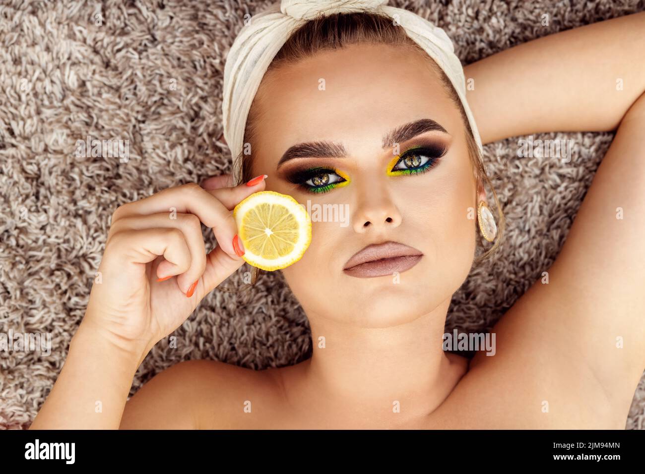 Beauty and skin care concept with gorgeous woman with perfect makeup covering one eye with organic lemon Stock Photo