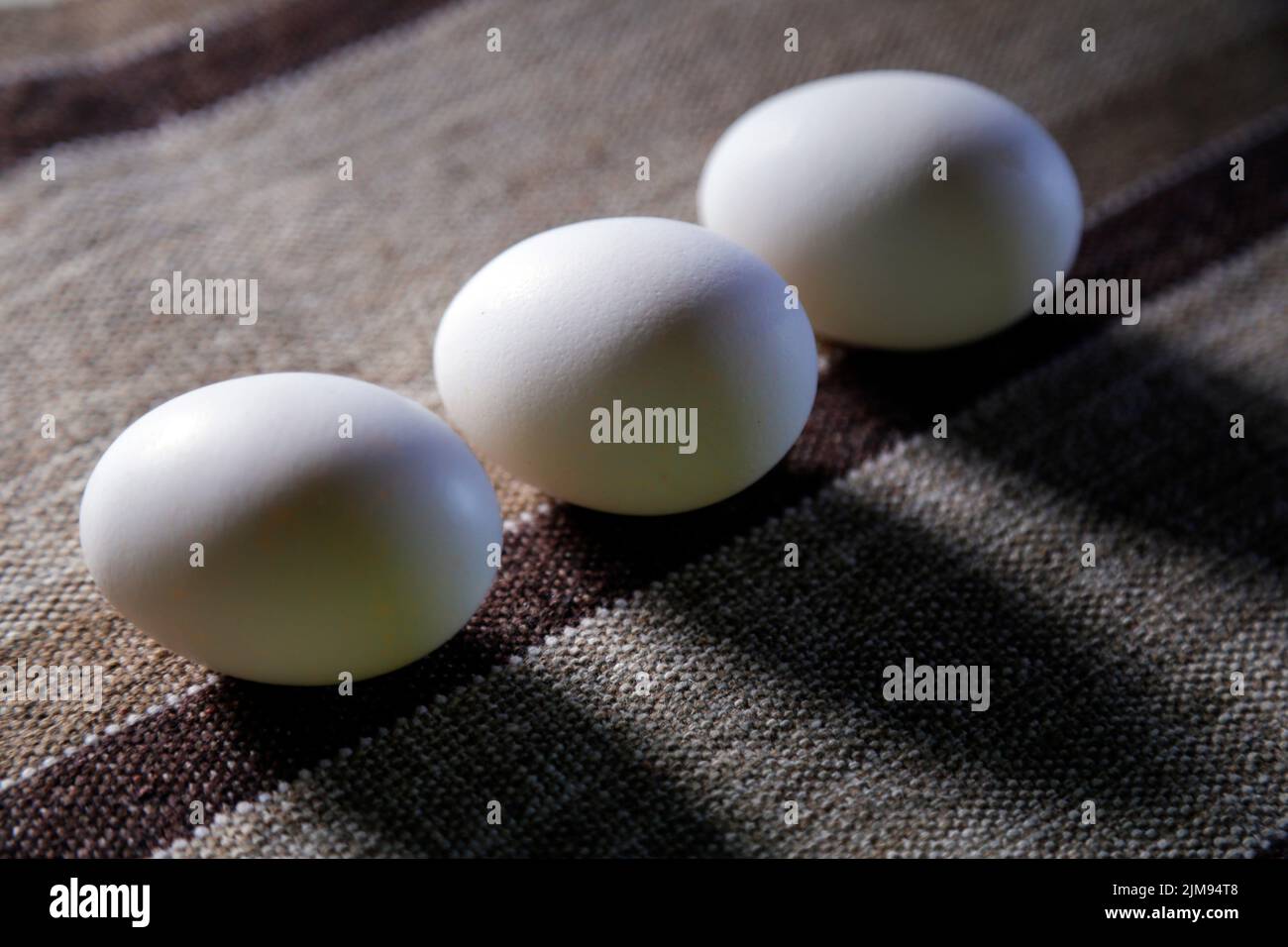 three white eggs grouped on top of fabric and soft side lighting - selective focus Stock Photo