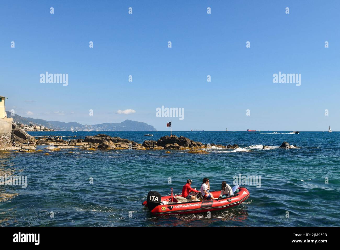 Two young couples sailing on a dinghy with the promontory of Portofino in the background, Boccadasse, Genoa, Liguria, Italy Stock Photo