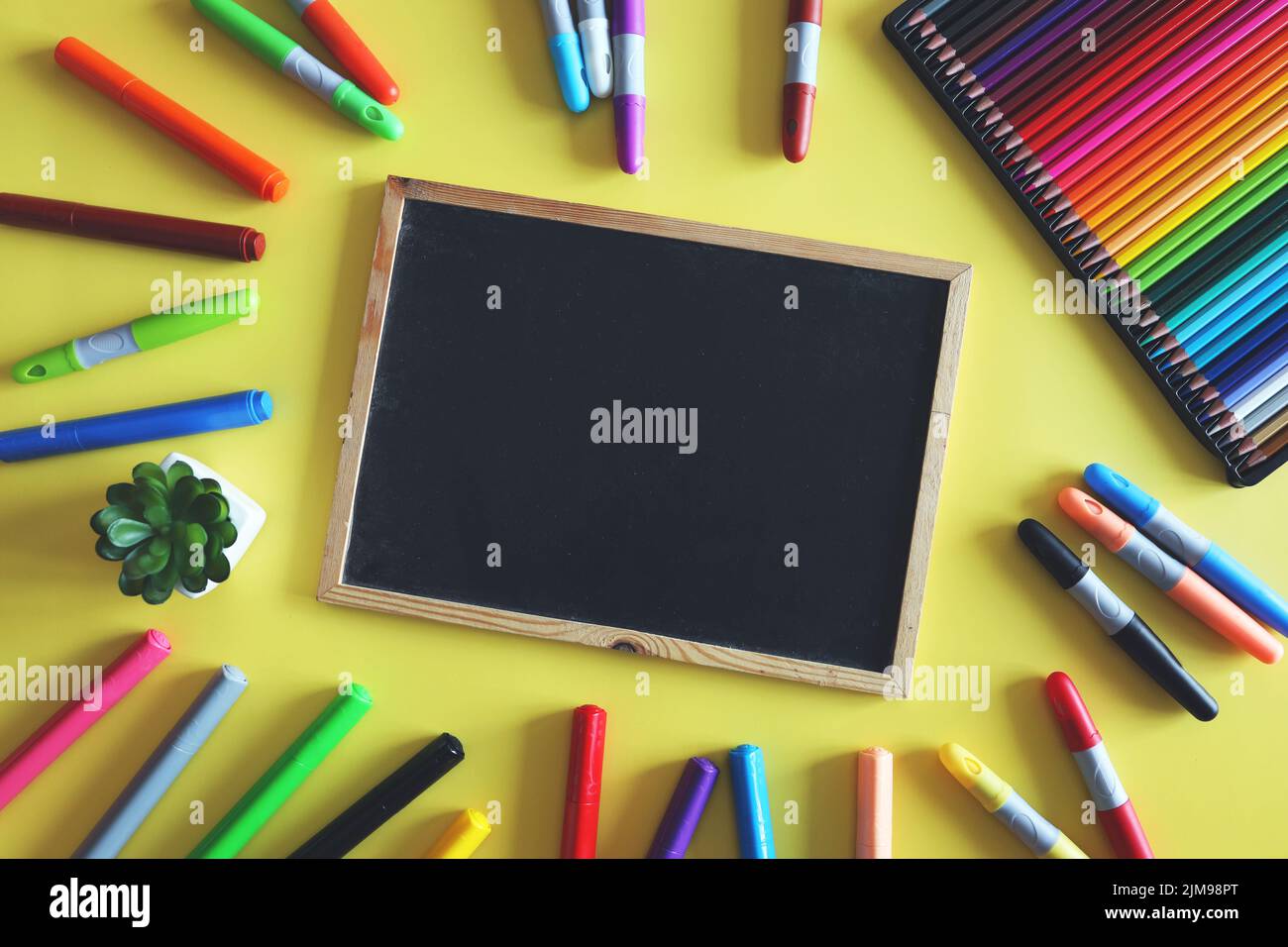 https://c8.alamy.com/comp/2JM98PT/chalk-board-with-colored-markers-and-pencils-on-yellow-background-school-supplies-for-kids-top-view-2JM98PT.jpg