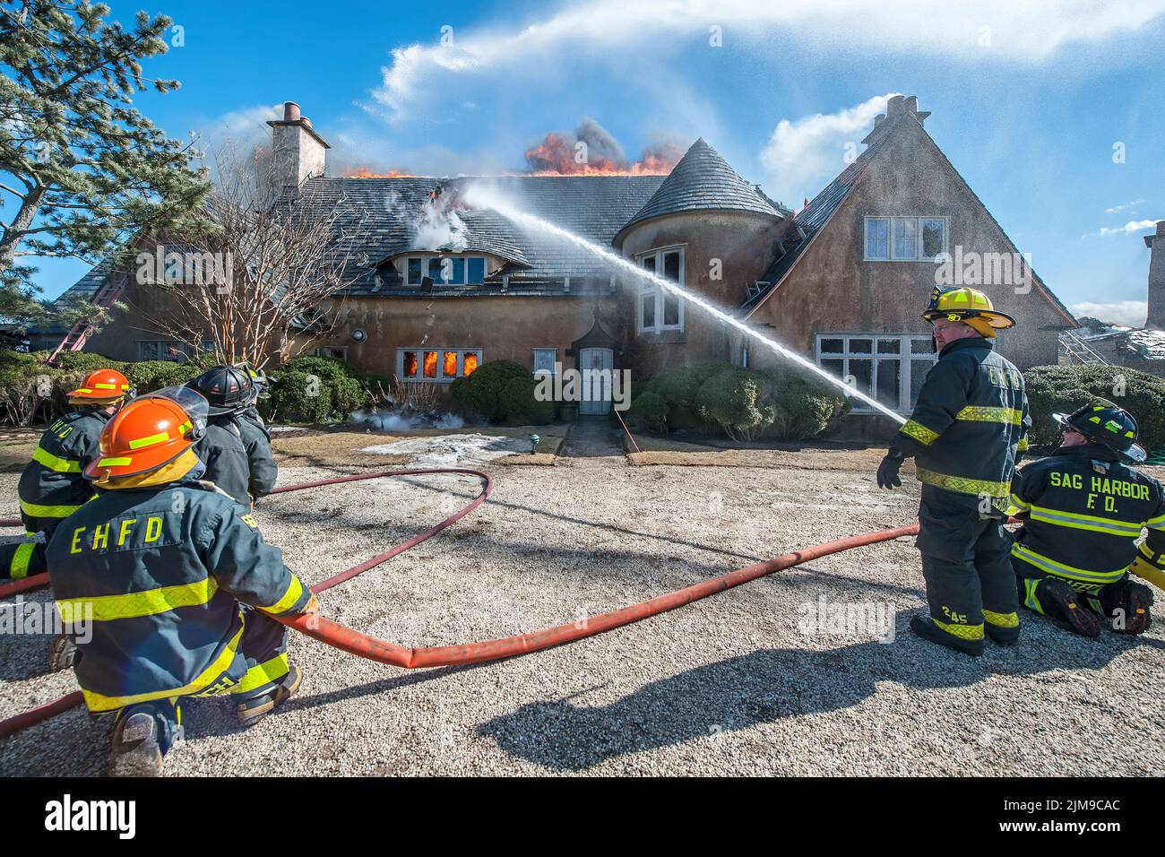 An East Hampton and Sag Harbor firefighter train hoses onto the roof of the house as East Hampton, New York firefighters are assisted by several neigh Stock Photo