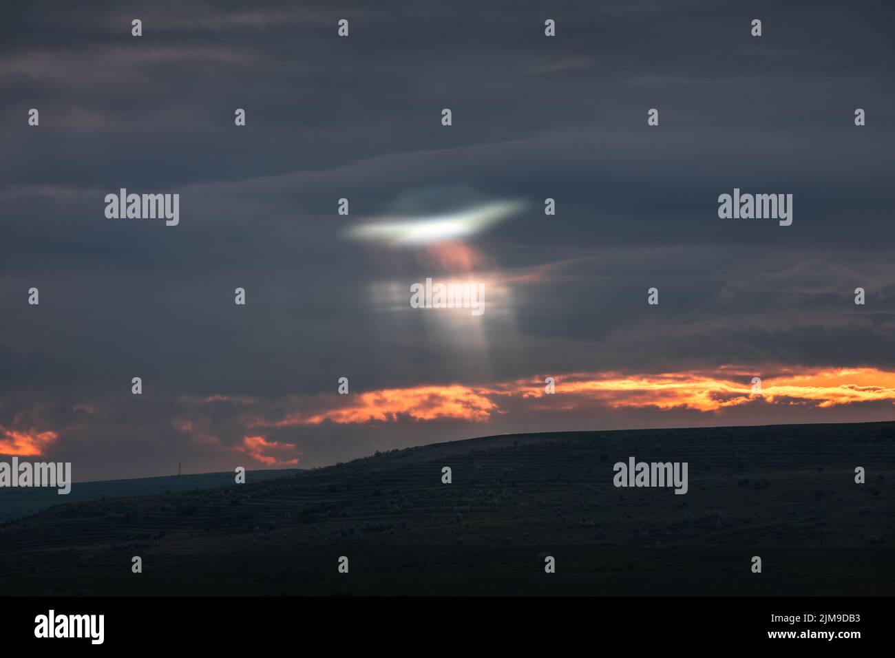 UFO shape lights that is seen passing through the dark clouds. Composit image, UFO shape light was added in post processing to the image. Stock Photo