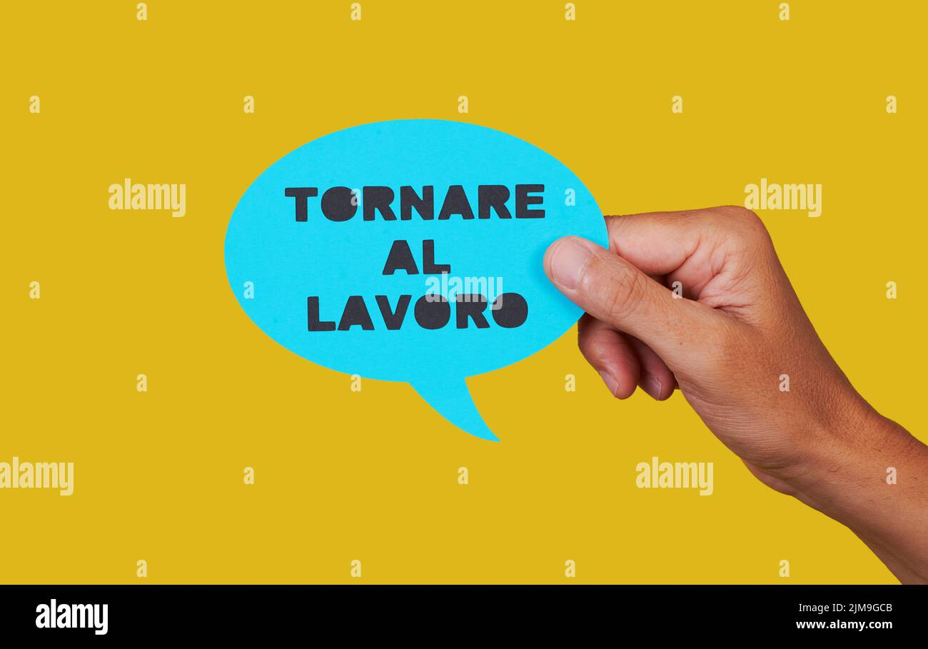 closeup of a man holding a blue paper speech bubble with the text back to work written in italian, on a yellow background Stock Photo